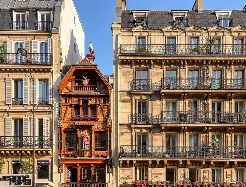 Photographie : une étroite façade à colombages et à pignons, entre deux immeubles haussmanniens