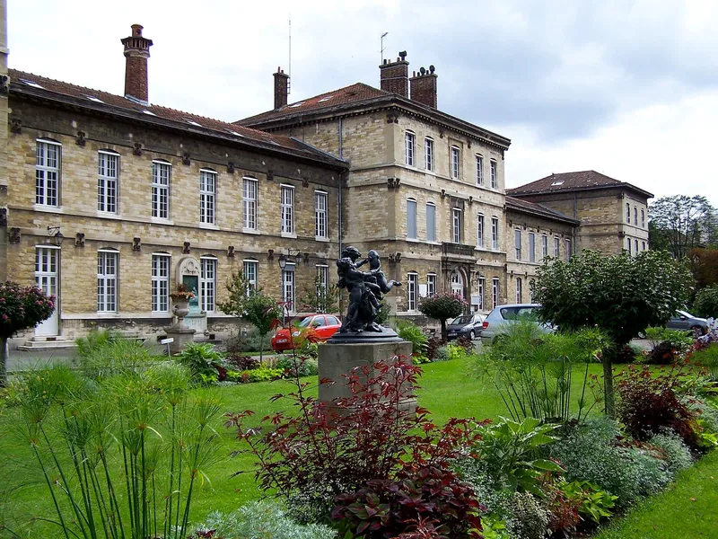 Photographie : un long pavillon de pierre derrière un jardin fleuri et une statue