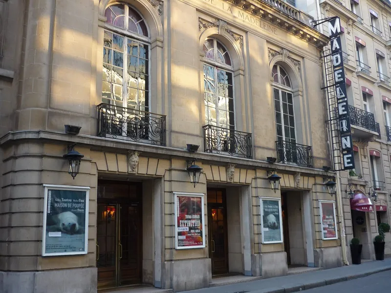 Photographie : la façade classique du théâtre, avec ses affiches et son enseigne verticale « Madeleine »