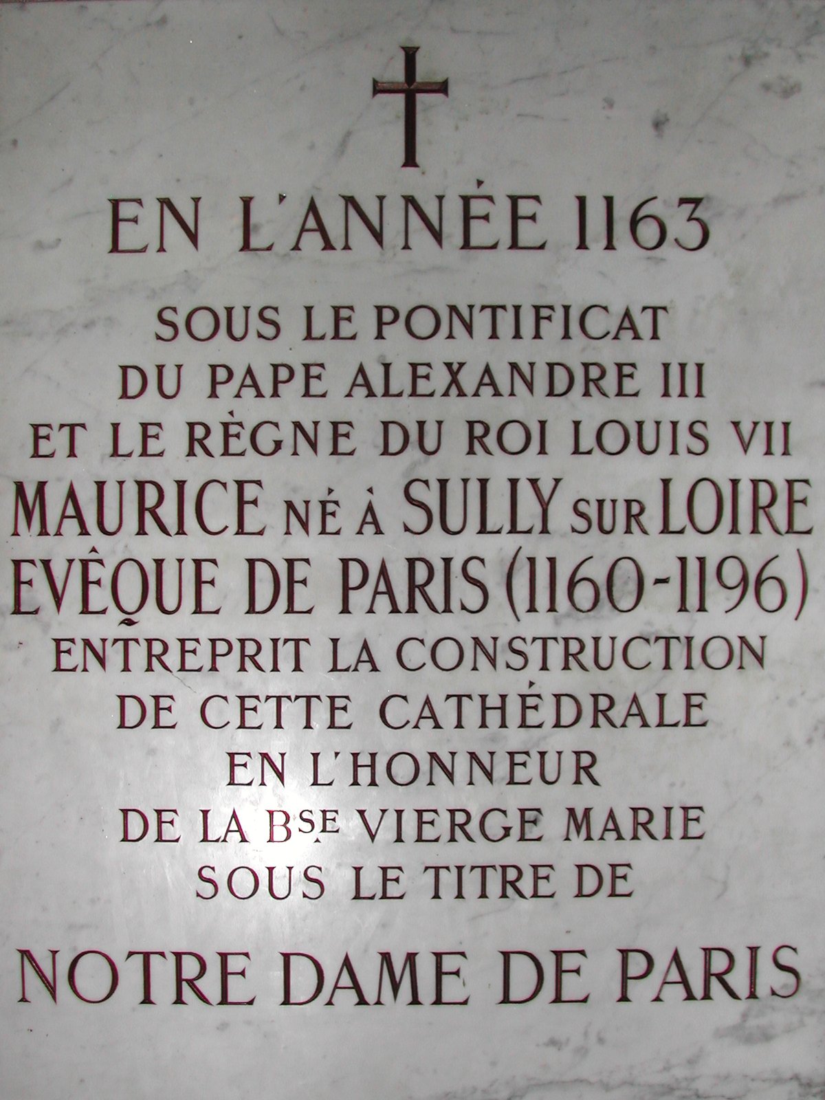 Plaque de marbre gravée de lettres rouges et noires, surmontée d’une croix