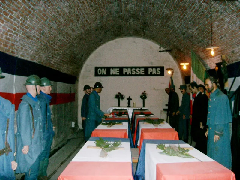 Photographie : des mannequins en uniforme bleu horizon devant des cercueils drapés de tricolore, dans une galerie voûtée
