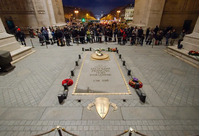 Photographie : la dalle du Soldat inconnu, fleurie, la flamme allumée, sous l'Arc de triomphe, un soir d'hiver