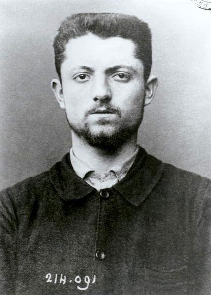Émile Henry photographié après son arrestation, en 1894 — anonyme · domaine public — Wikimedia Commons Photographie anthropométrique : Émile Henry de face, jeune homme aux cheveux courts et à la barbe naissante, en veste sombre, un numéro inscrit en bas