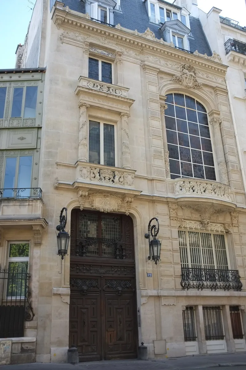 Photographie : une façade étroite de pierre sculptée, avec une grande baie vitrée et une porte cochère