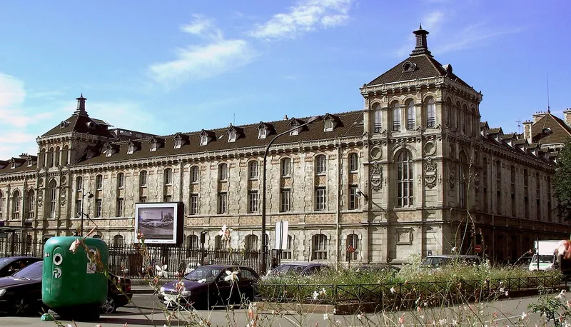 Photographie : une longue façade polychrome de brique et de pierre, avec des tours carrées à lanternon