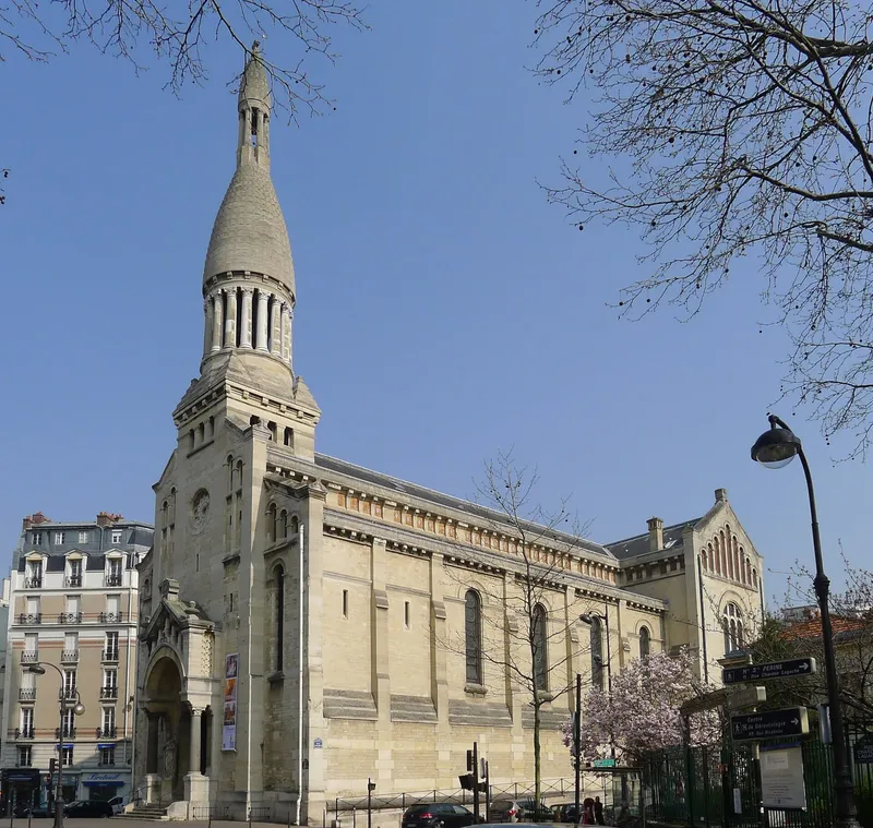 Photographie : une église de pierre claire à clocher pointu, au coin d'une place