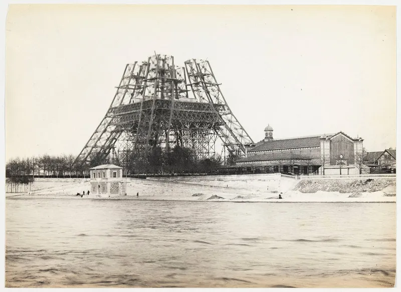Photographie : la tour Eiffel en chantier, au-dessus du premier étage, vue de l'autre rive de la Seine