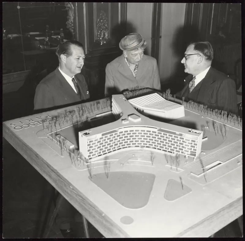 Photographie en noir et blanc : Eleanor Roosevelt, entre deux hommes en costume, se penche sur la maquette blanche du futur siège en étoile