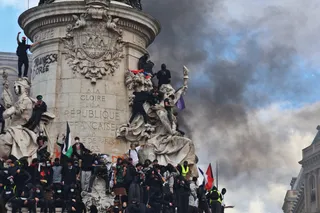 Des manifestants, pour beaucoup masqués, escaladent le monument à la République sous un nuage de fumée noire