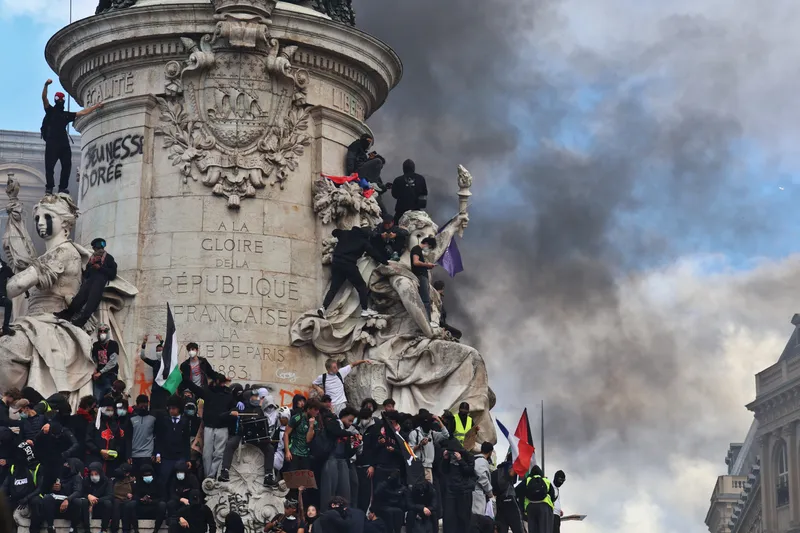 Des manifestants, pour beaucoup masqués, escaladent le monument à la République sous un nuage de fumée noire