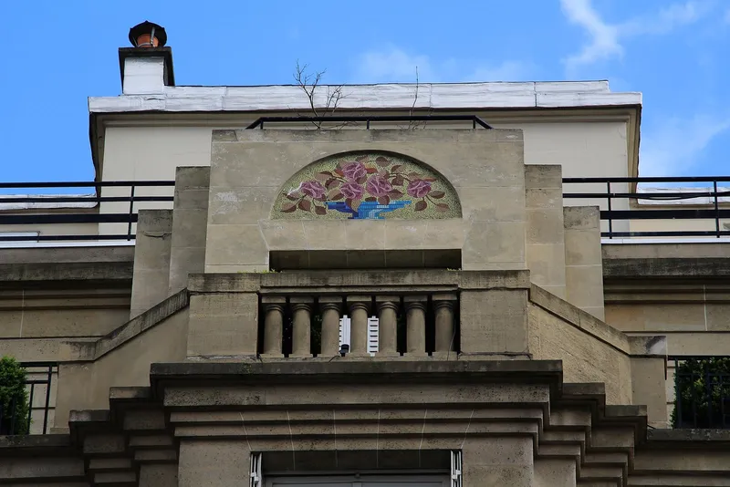 Photographie : une façade de pierre Art déco, avec une mosaïque fleurie en demi-cercle au-dessus d'un balcon