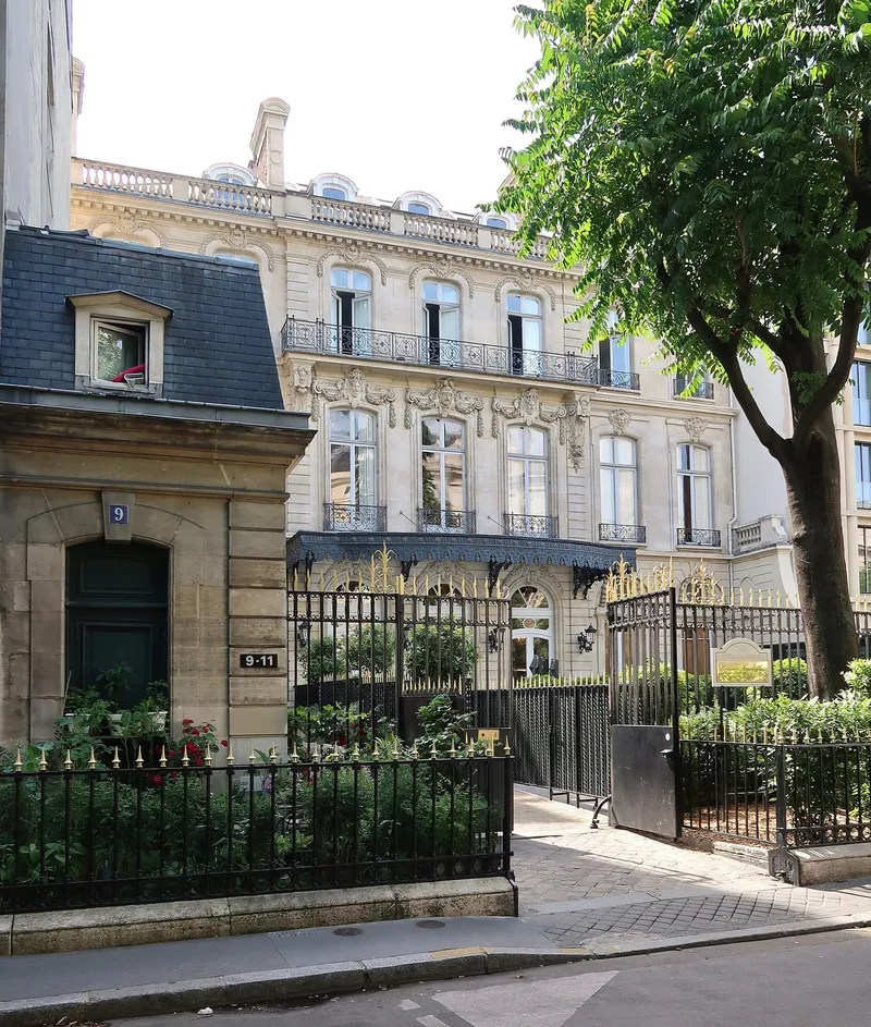 Photographie : un hôtel particulier de pierre derrière une grille et des arbres