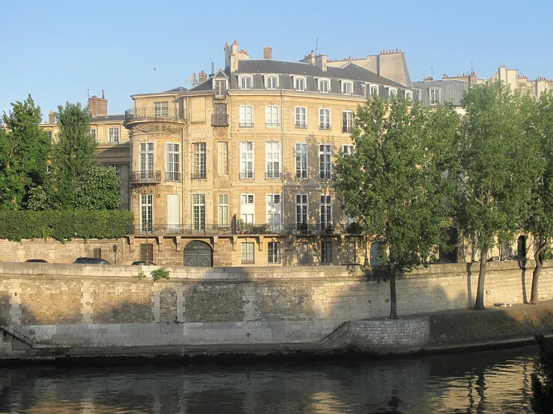 Photographie : la façade de l'hôtel Lambert au-dessus du quai, derrière les arbres, au bord de la Seine