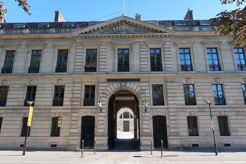 Photographie : une longue façade classique de pierre, avec un grand portail en arc au centre
