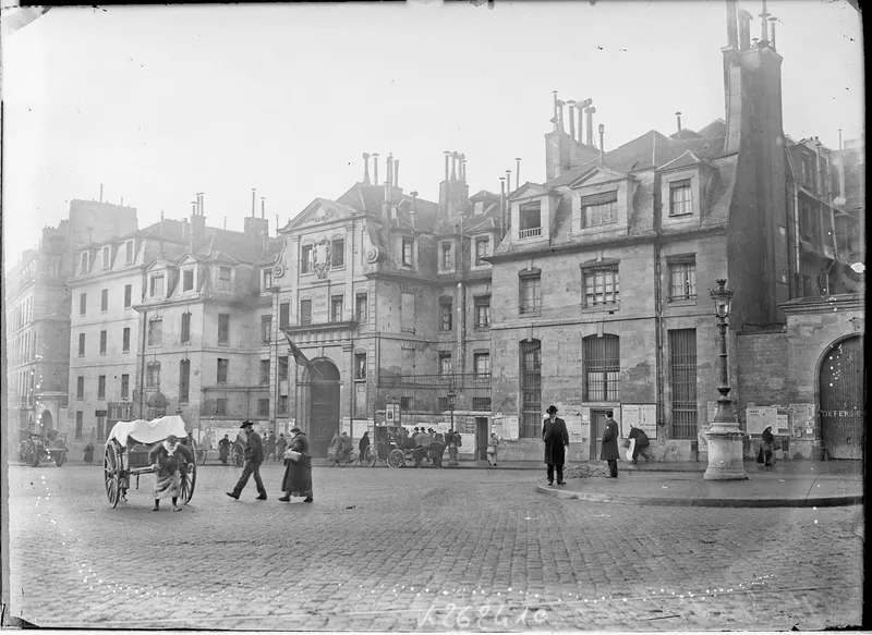 Photographie ancienne : des passants et une voiture à cheval devant les bâtiments de la prison