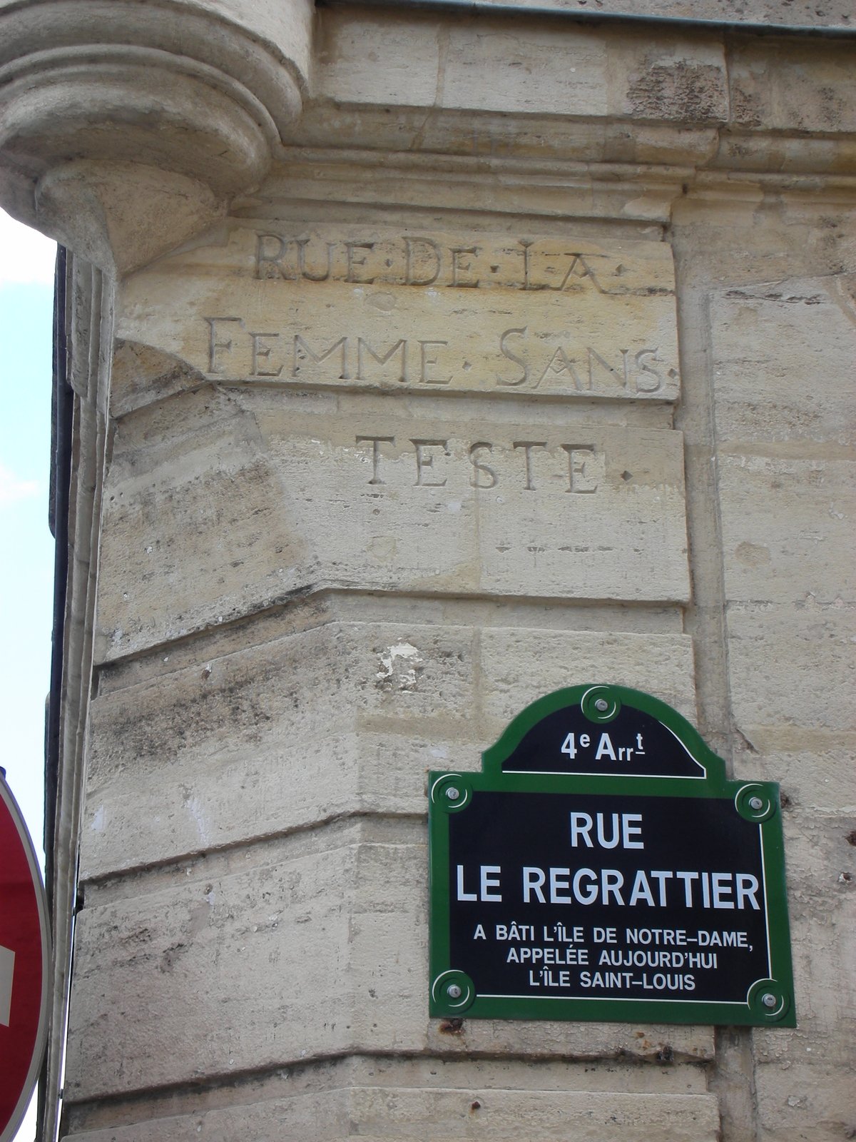 À l’angle de la rue Le Regrattier et du quai de Bourbon, l’ancien nom gravé dans la pierre, « Rue de la Femme sans teste » — Photo Philippe Boisseau — Archives Paris révolutionnaire Photographie : à l’angle d’un immeuble de pierre, l’inscription gravée « Rue de la Femme sans teste » au-dessus de la plaque émaillée « Rue Le Regrattier »
