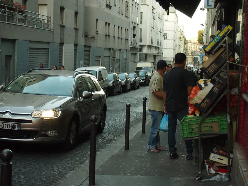 Photographie : la rue de Chartres, étroite et pavée, des voitures garées et les étals d’un commerce sur le trottoir