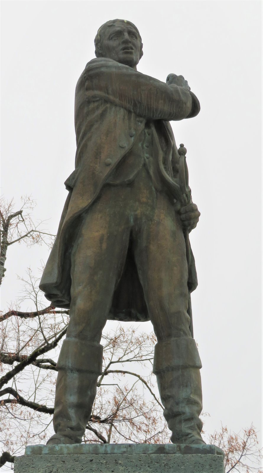 La statue de Pierre-Nicolas Chenaux devant le château de Bulle, en Gruyère — Temosis · CC BY-SA 4.0 — Wikimedia Commons Statue de bronze d'un homme en habit du XVIIIe siècle, debout, les bras croisés, sur un socle de pierre