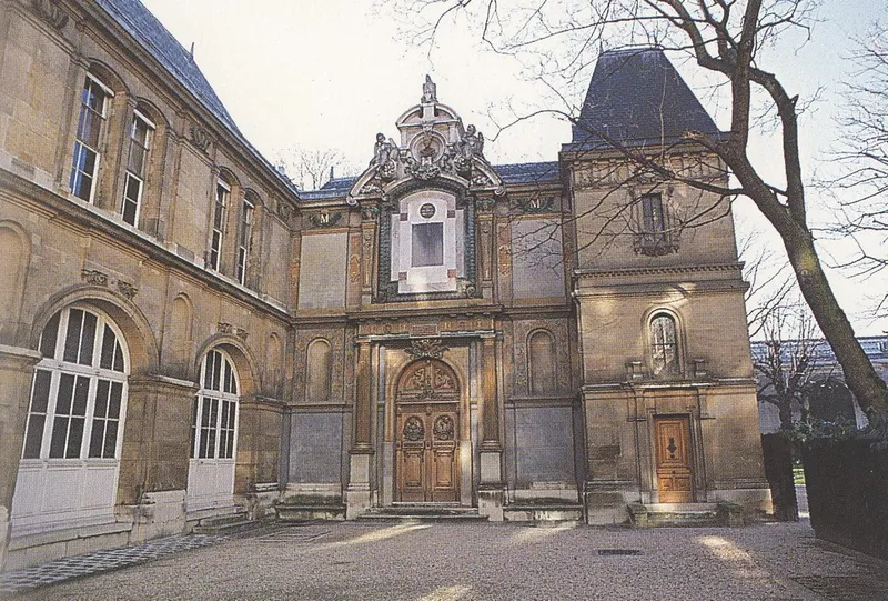 Photographie : la cour d’un hôtel classique, avec un portail sculpté et deux ailes à hautes fenêtres