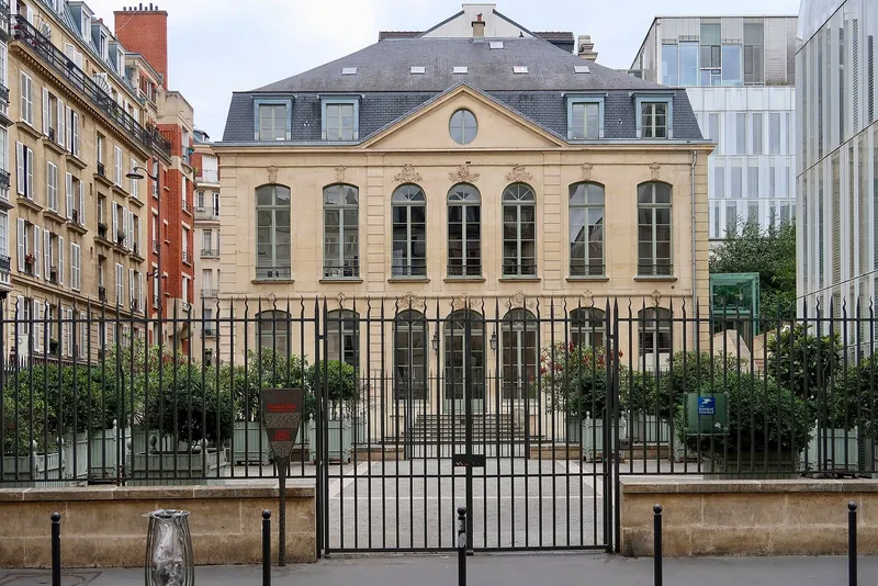 Photographie : un hôtel du XVIIIe siècle derrière une grille, entre des immeubles