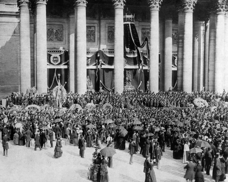 Photographie : la colonnade du Panthéon tendue de draperies noires, devant une foule dense