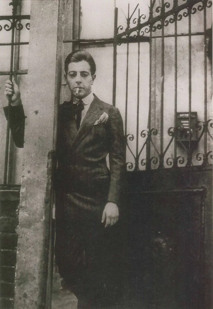 Jacques PRÉVERT. Devant la grille de la rue du Château, à Montparnasse